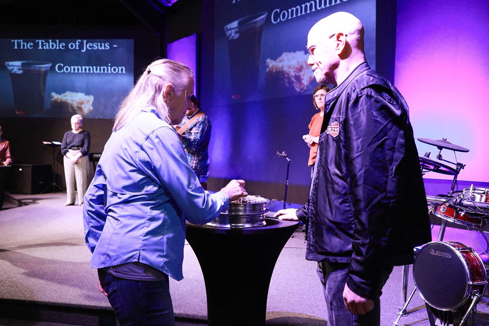 A black and white photo of a group of people standing in front of a stage.