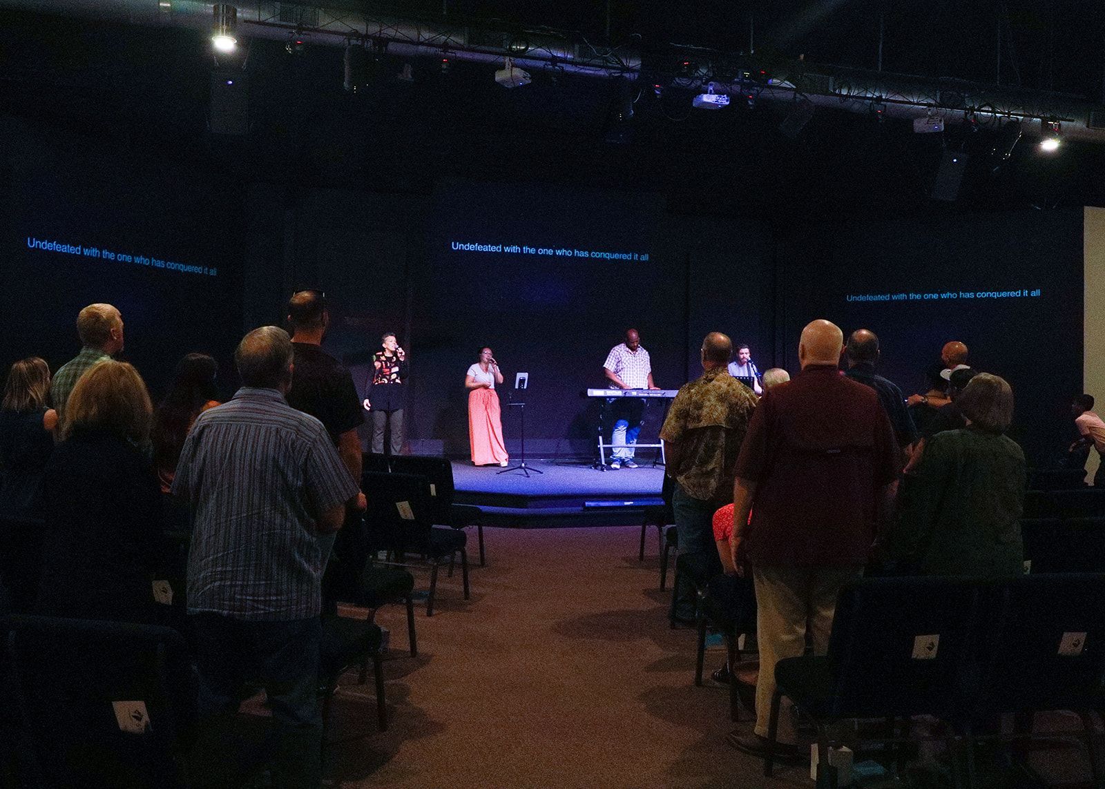 A group of people are sitting in front of a stage in a dark room.
