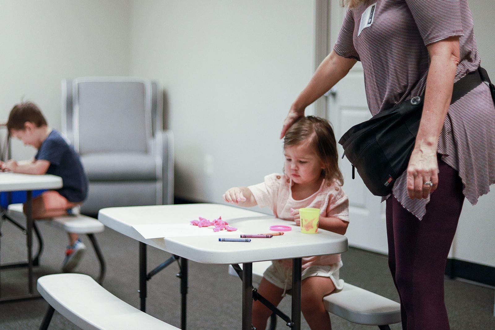 A woman is standing next to a little girl sitting at a table.