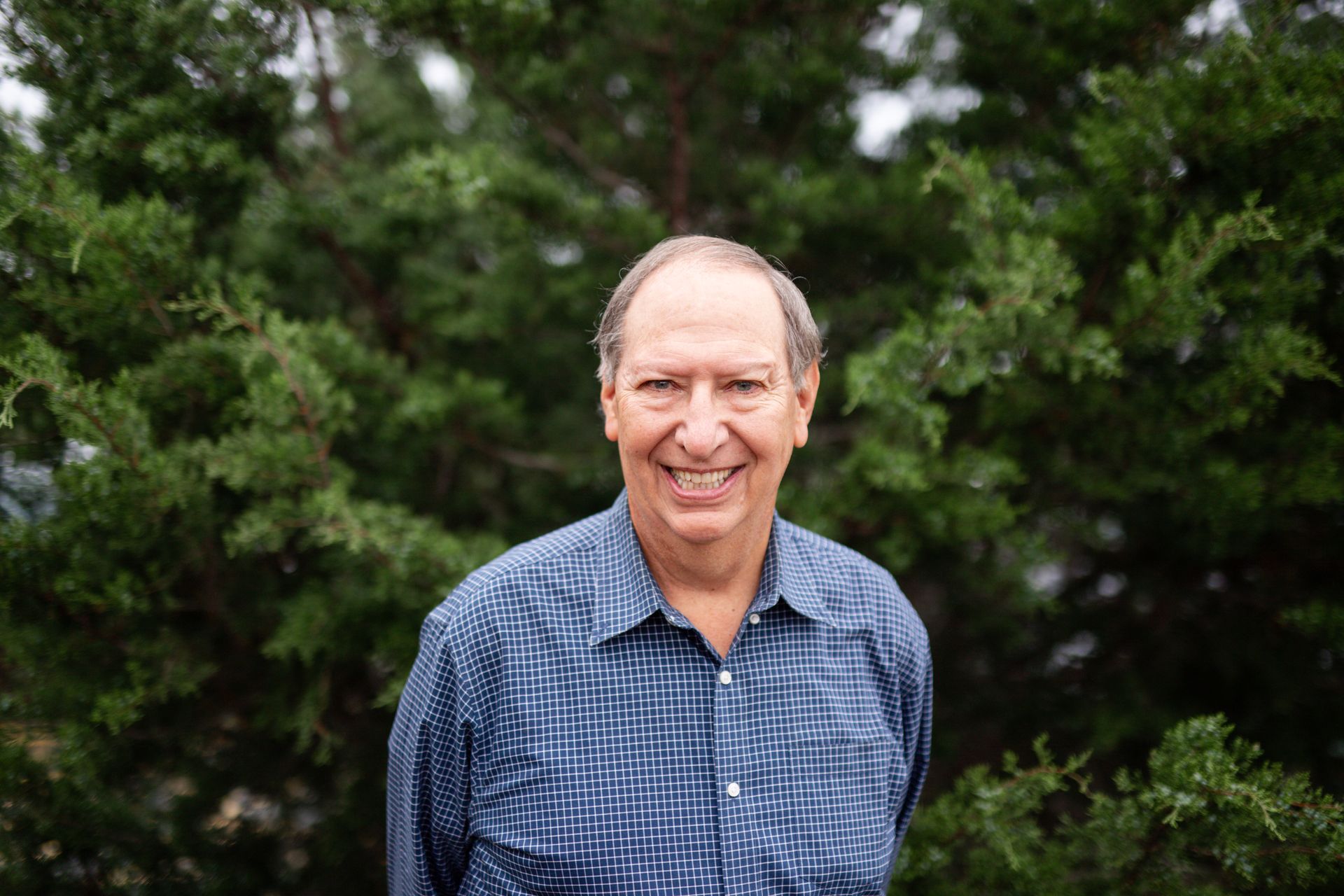 A man in a blue shirt is standing in front of a painting of a sailboat in the ocean.