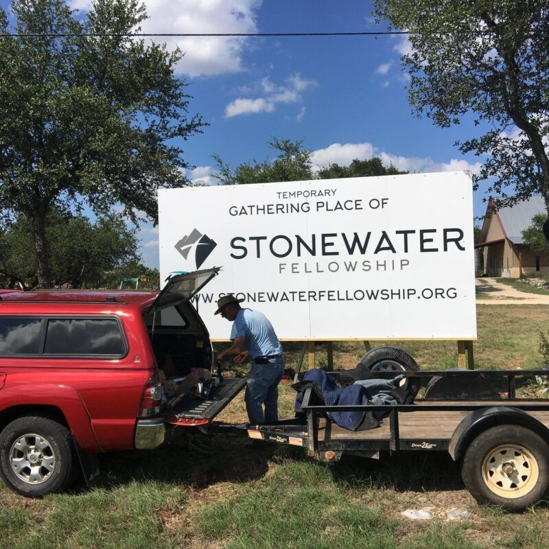 A red truck is parked in front of a sign for stonewater fellowship