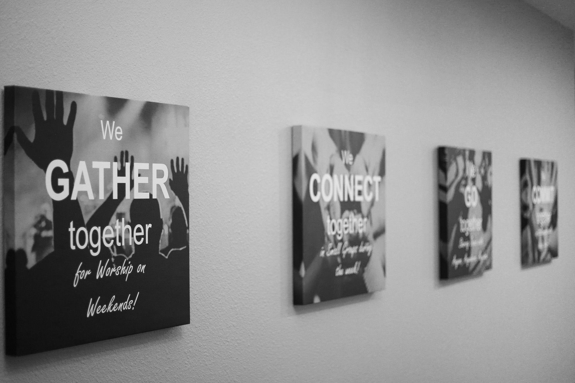 A black and white photo of a wall with a sign that says we gather together