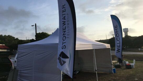 A white tent with a flag that says stonewater fellowship
