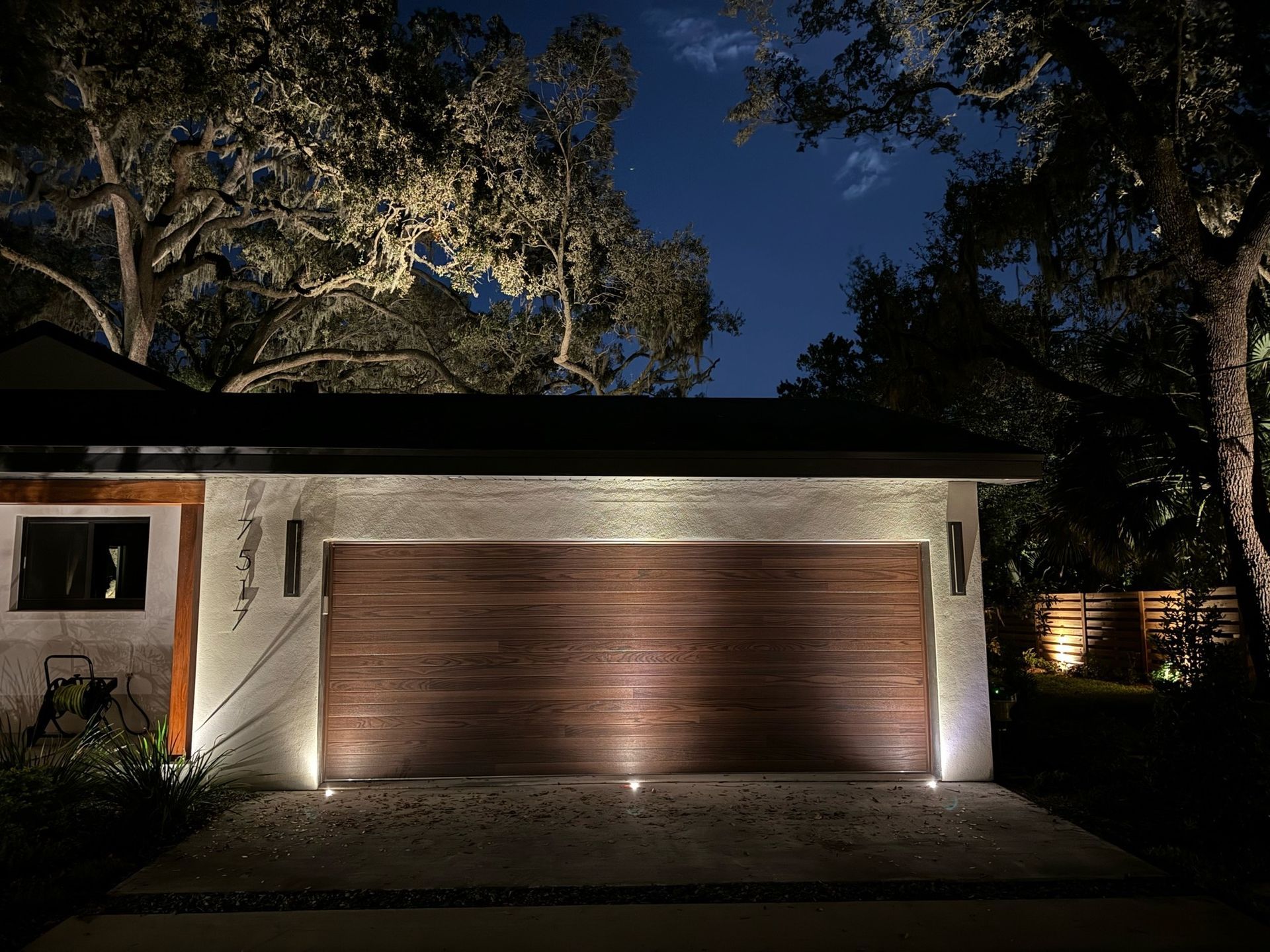 A garage door is lit up at night with trees in the background.