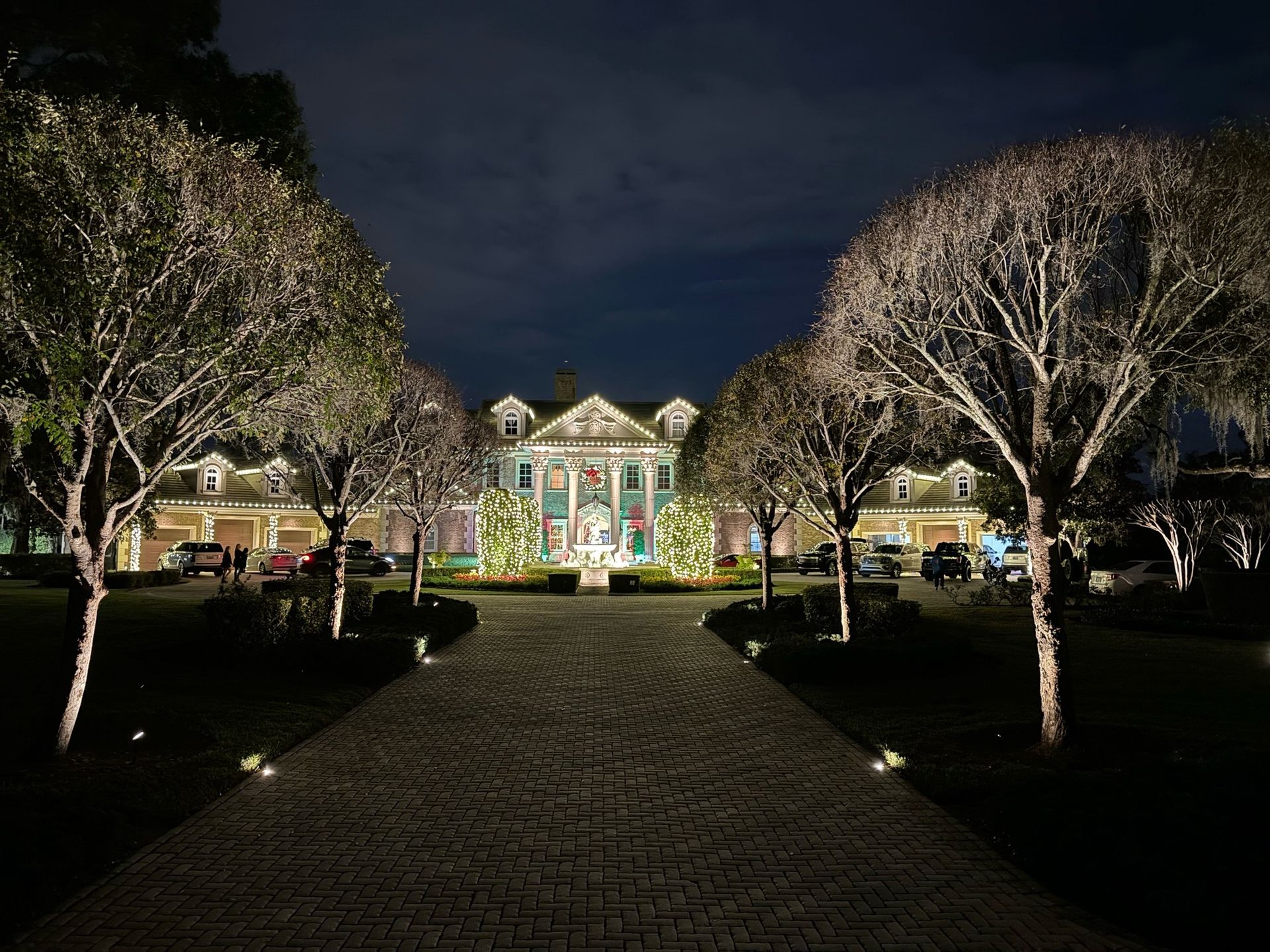 A large house is lit up at night with trees in front of it.