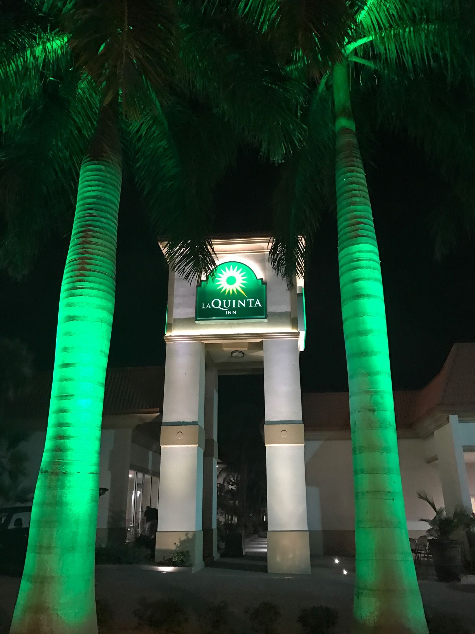 Two palm trees are lit up green in front of La Quinta Inn