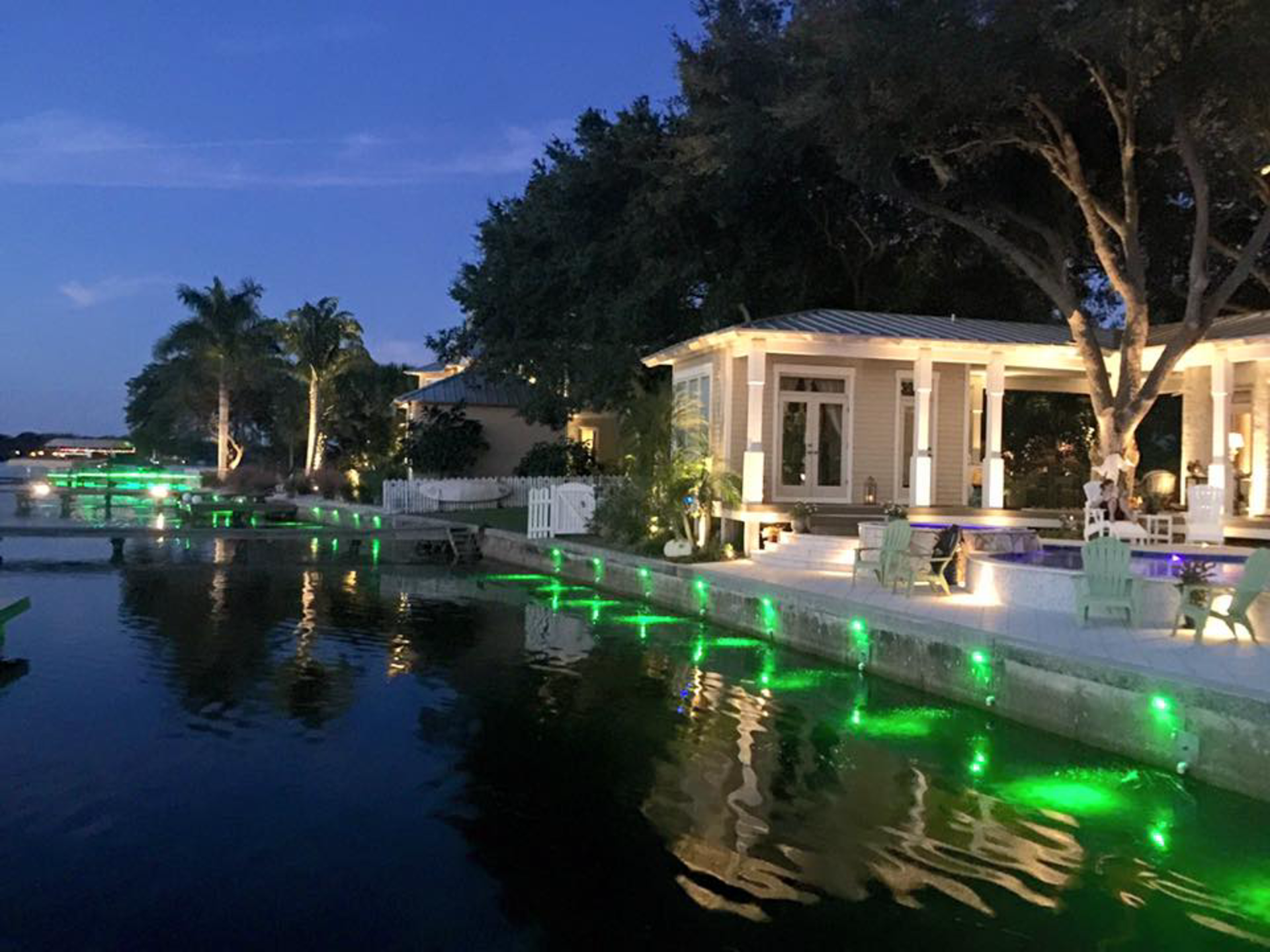 A dock with green lights on it and a house in the background.