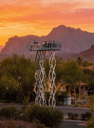 Raised observation platform at sunset in a desert landscape with mountains and warm orange sky