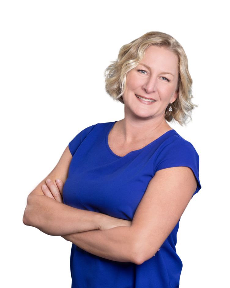 A woman in a blue shirt is standing with her arms crossed and smiling.