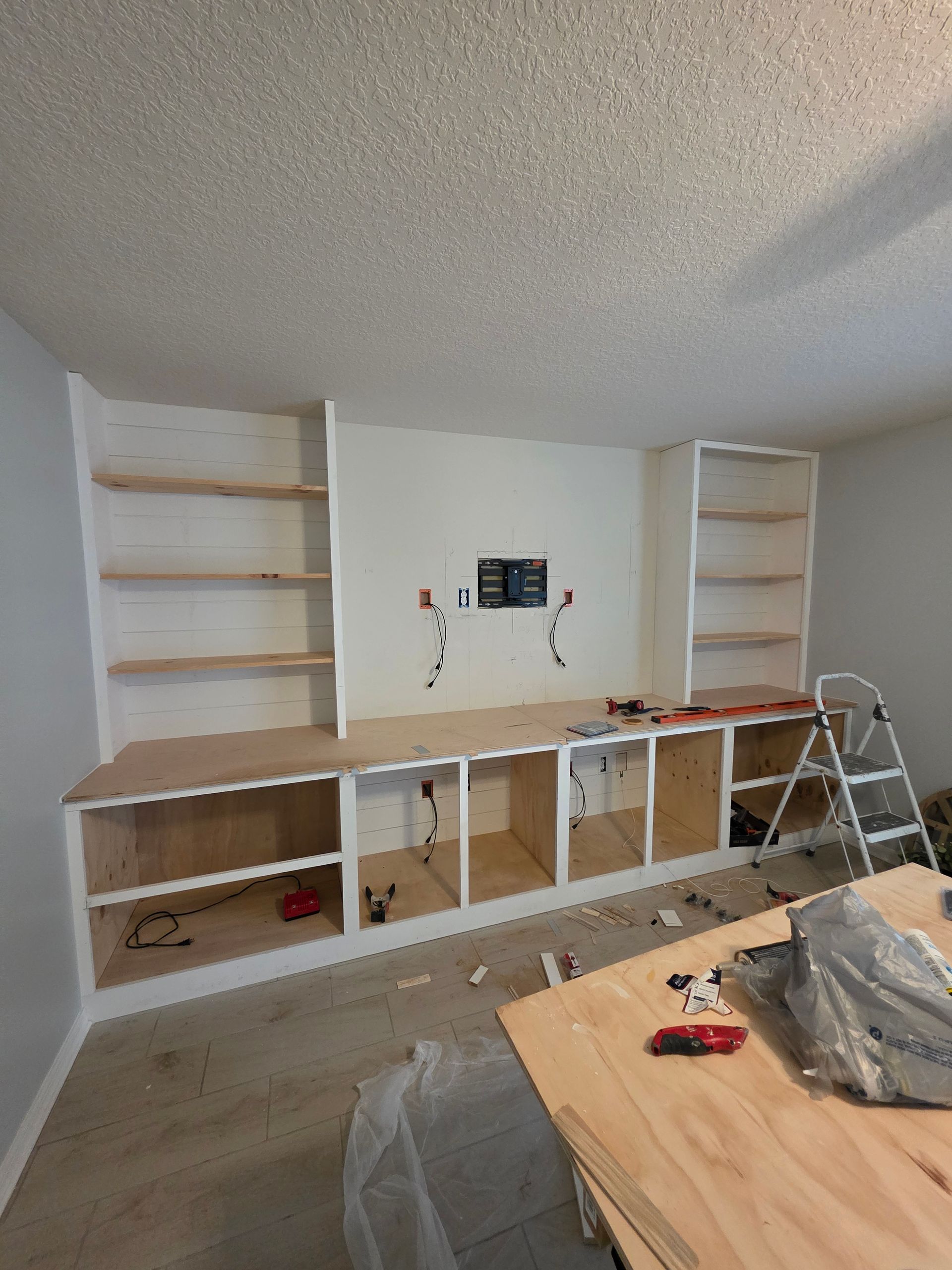 Built-in entertainment center under construction with shelves, cabinets, and a central space for a TV.