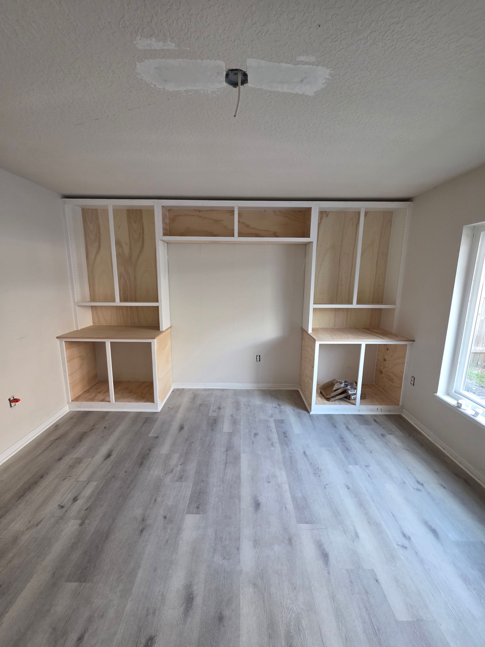 Built-in wooden cabinetry in a room with light grey flooring, white walls, and a ceiling light.