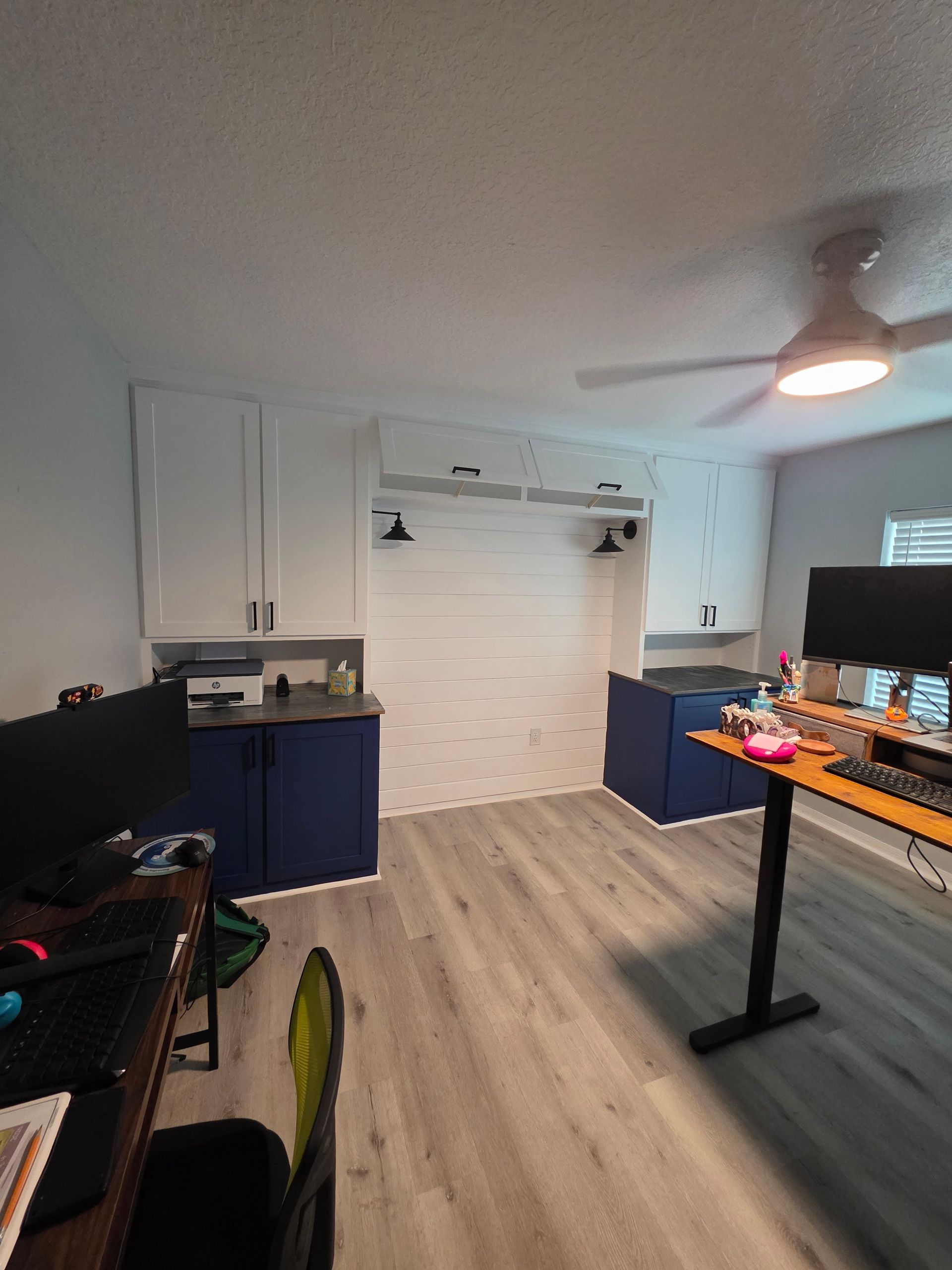 A small, modern home office space with blue and white cabinets, a desk, and a white-planked wall.