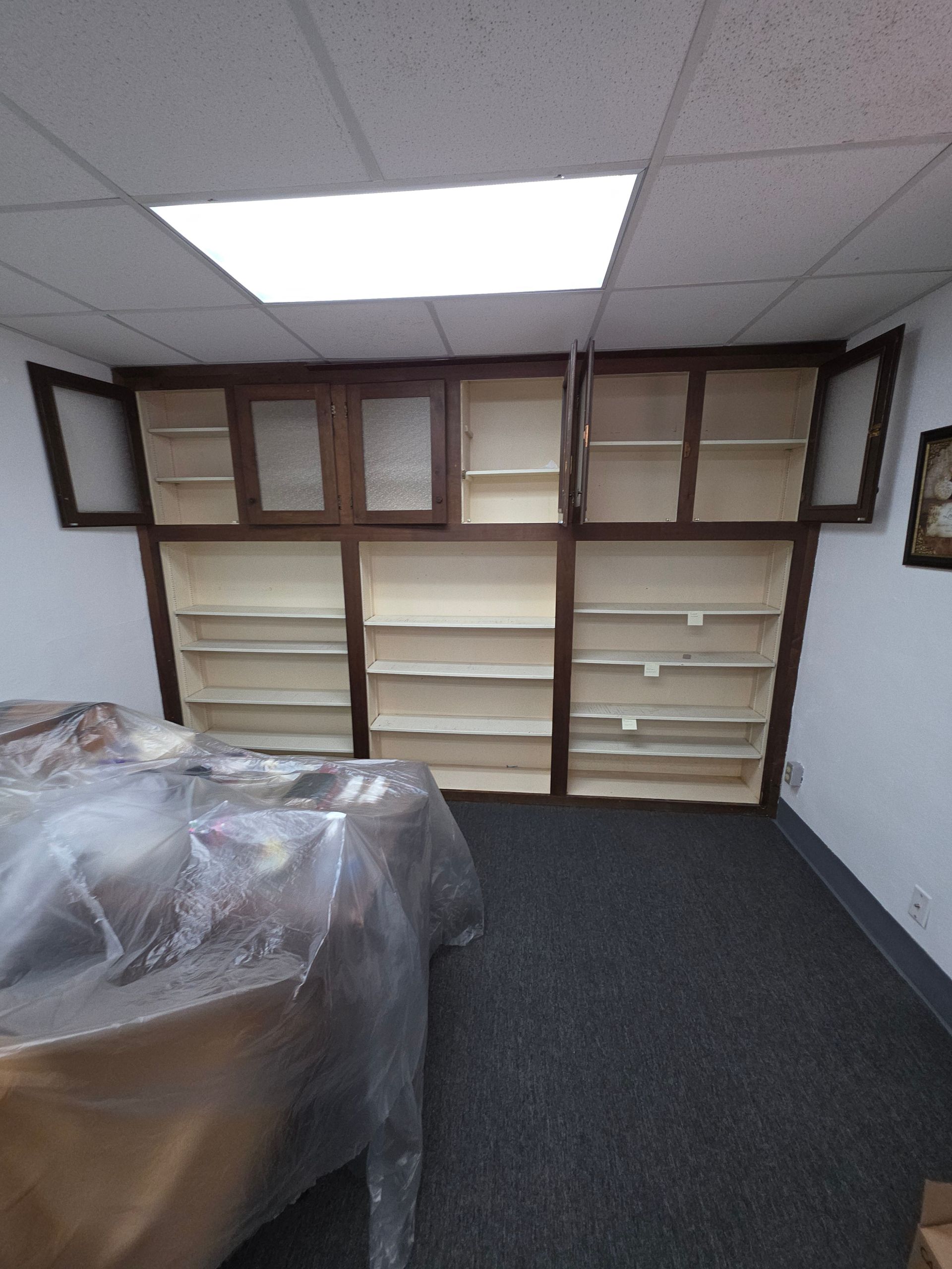 Built-in wooden shelves with cabinets on a white wall. The shelves are empty, and a table is in the foreground.