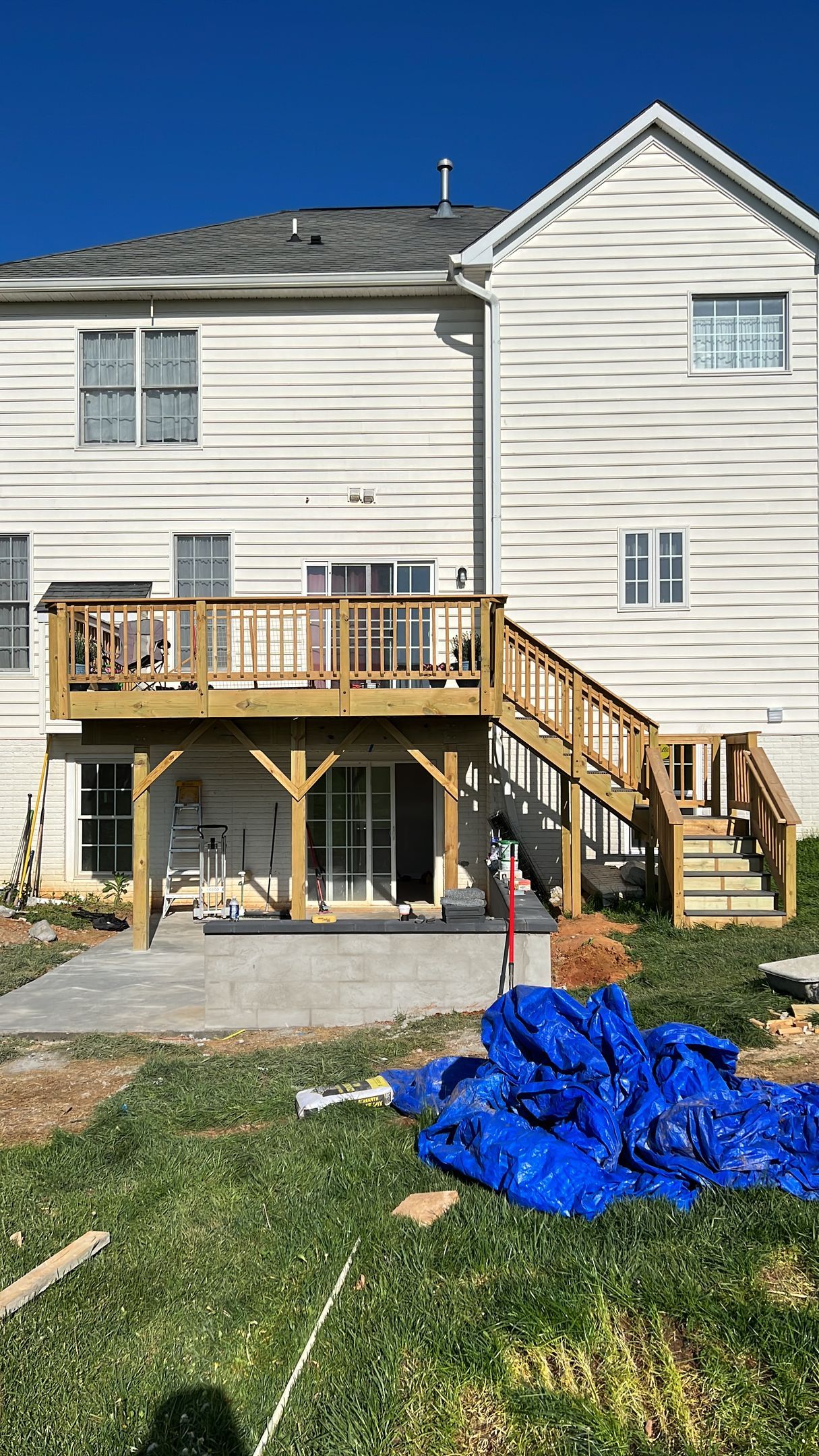 Wooden deck and stairs on a white house; construction site with blue tarp in the grass.