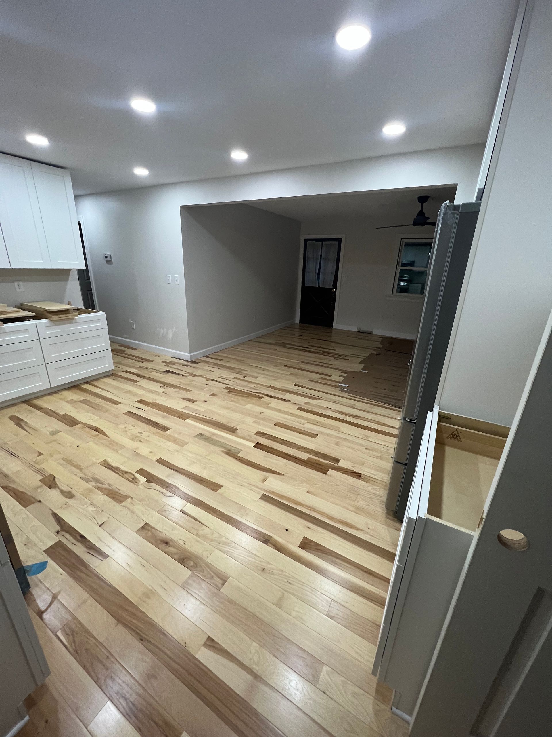 Room under renovation with wooden floors, gray walls, and bright overhead lights.
