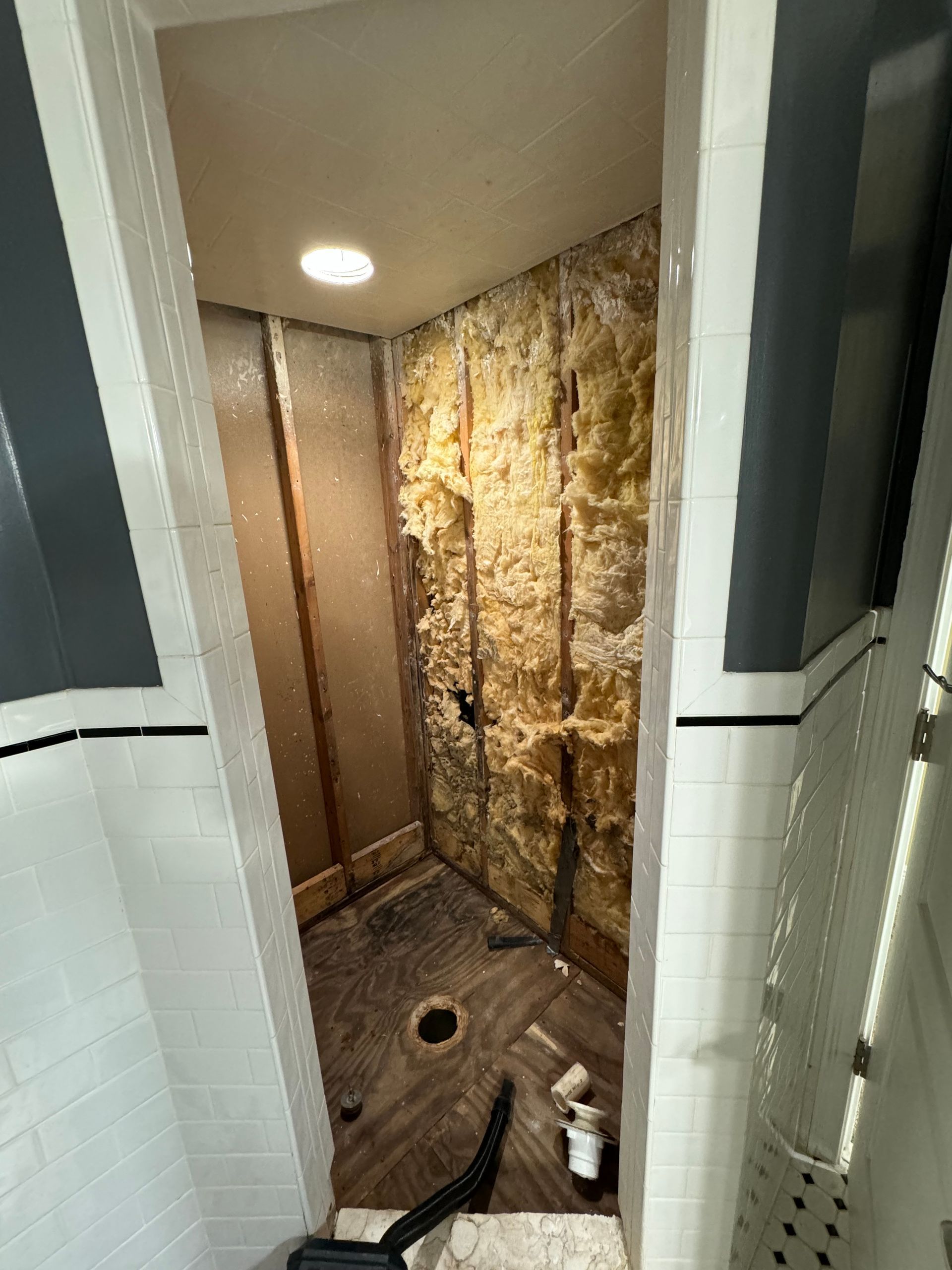 Shower with exposed wall showing insulation and damage.