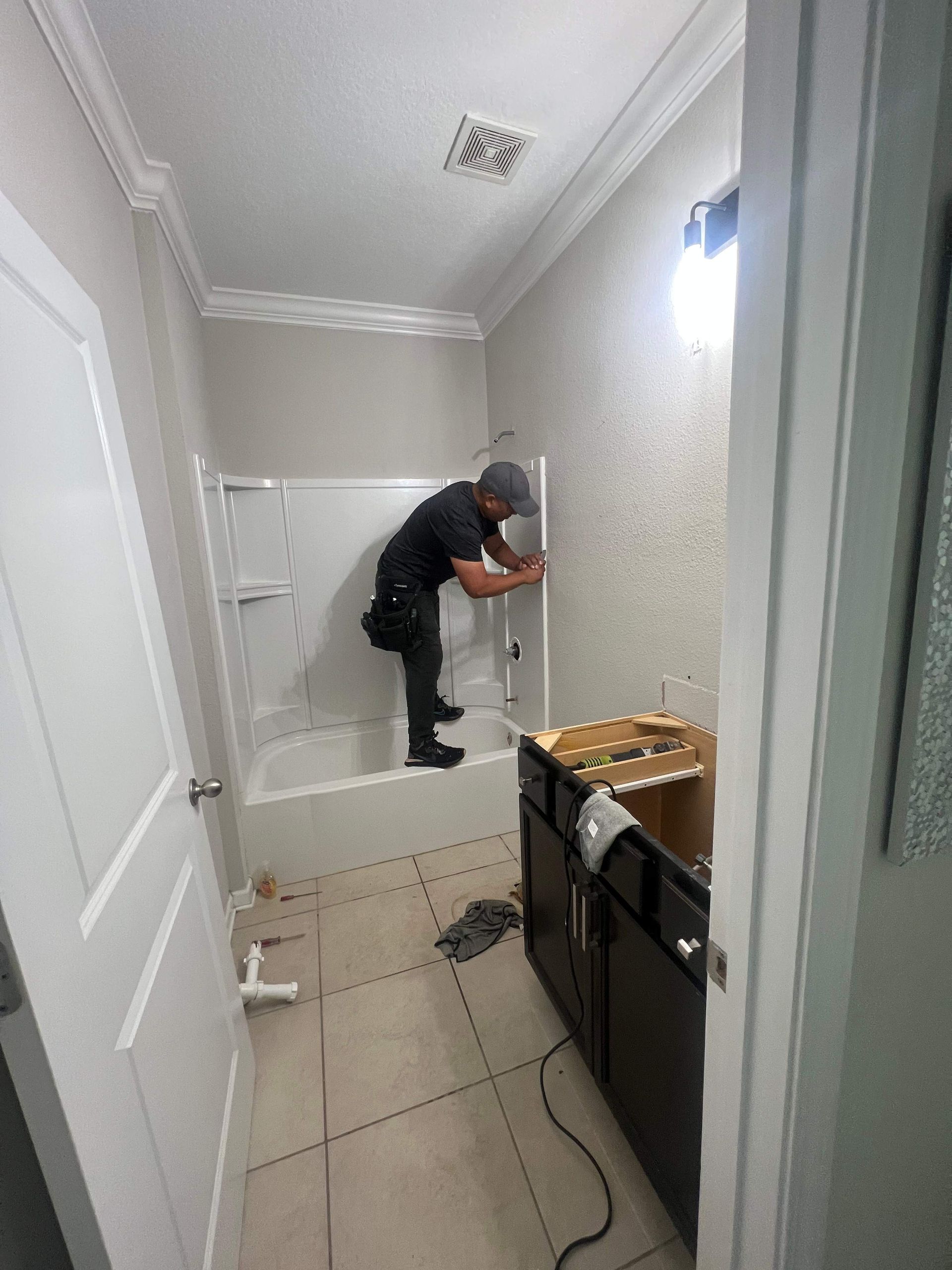 Person working in a bathroom, installing shower surround. Cabinet and door visible.