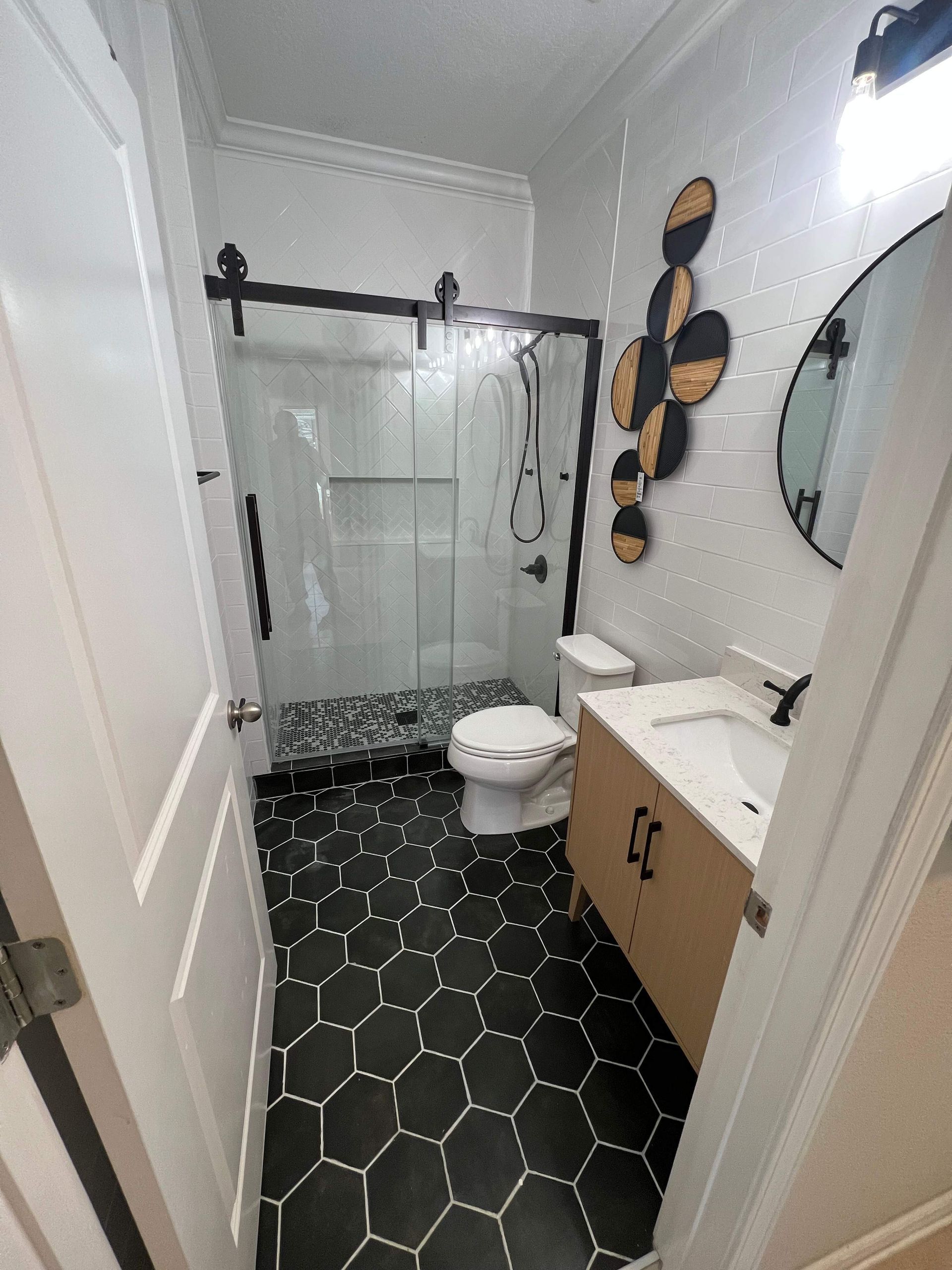 Small bathroom with black hexagon tile floor, glass shower, white walls, and a wood vanity.