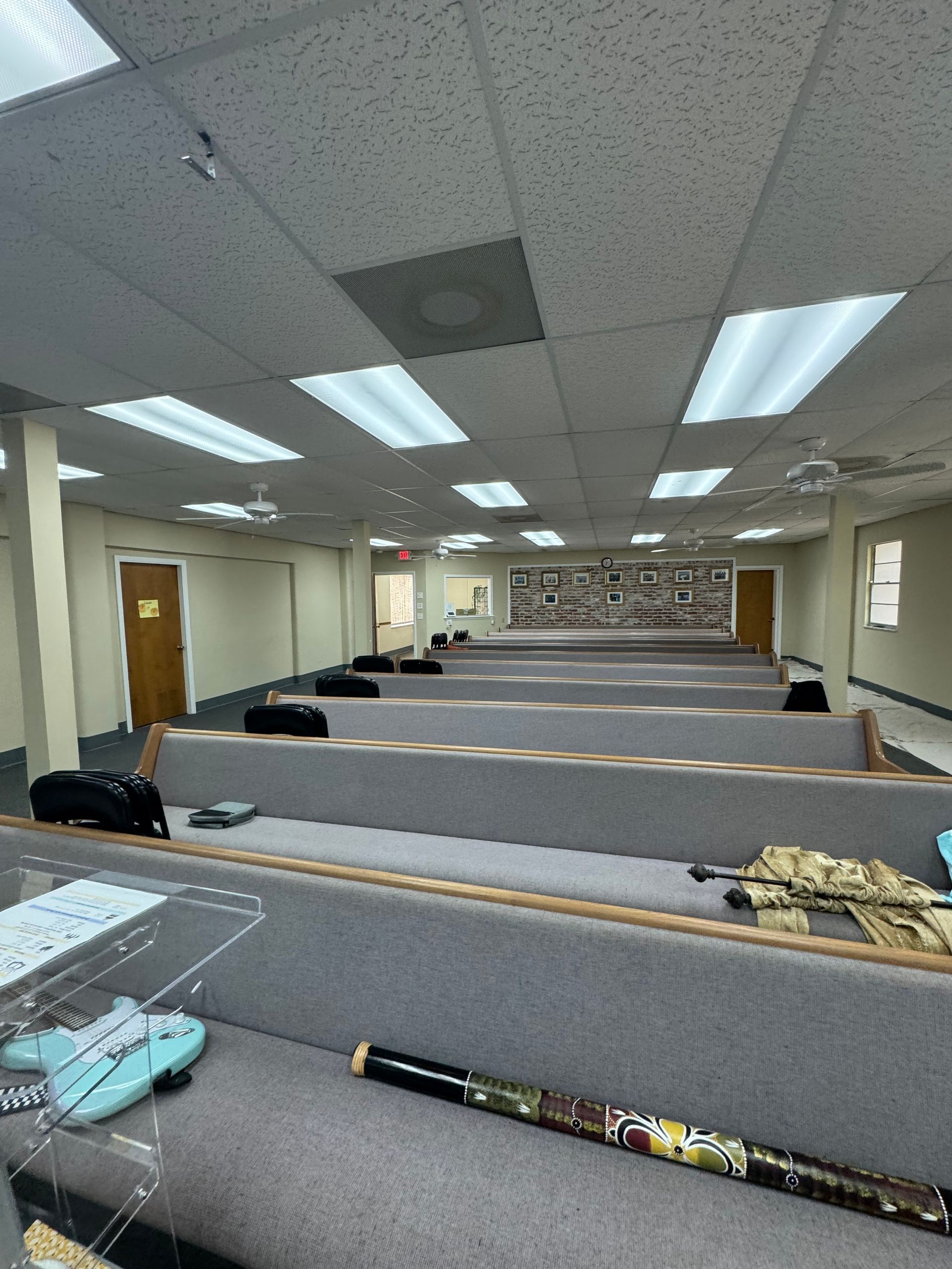 Empty room with rows of gray seating, fluorescent lights, and two closed doors.