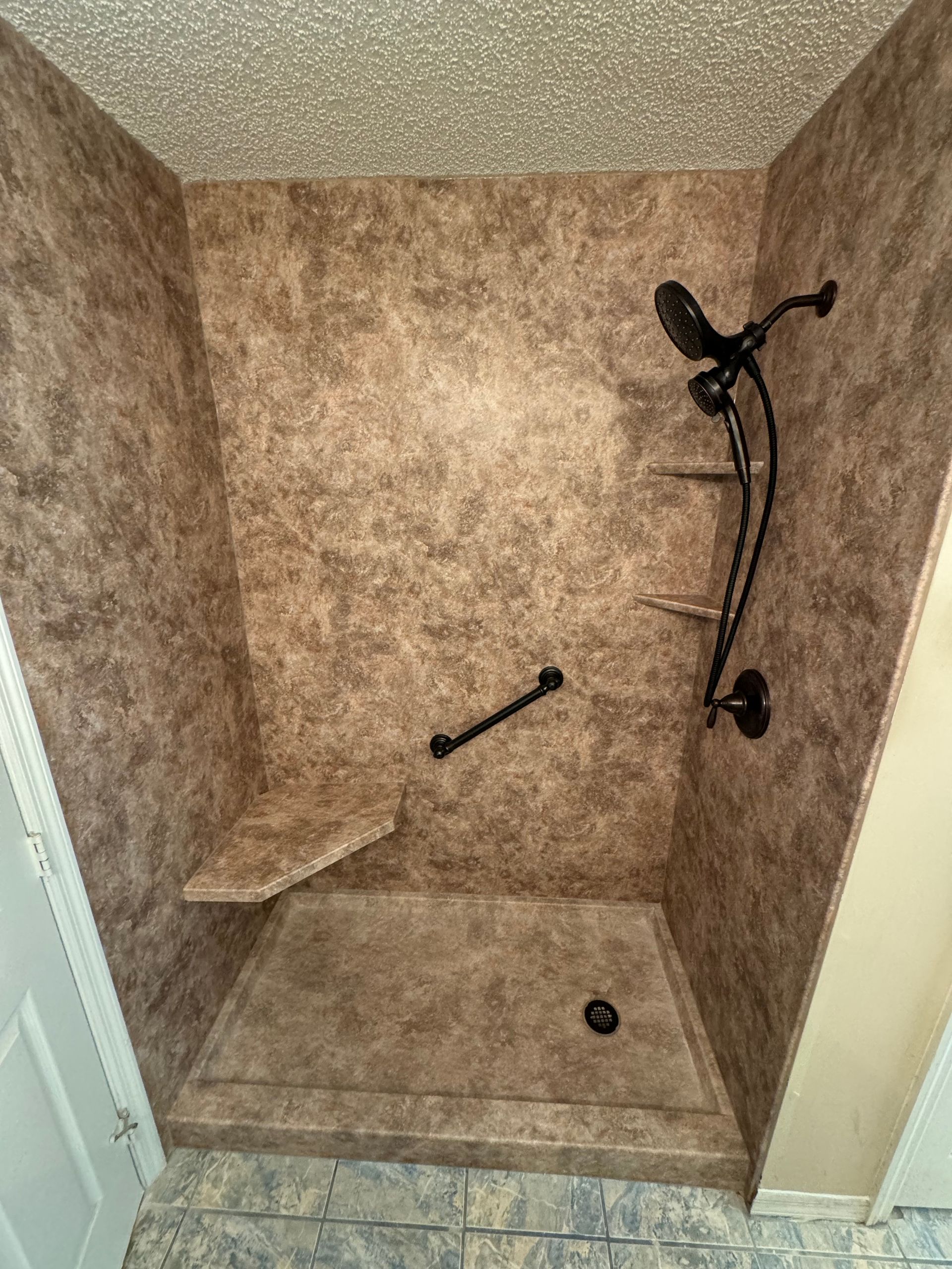 Brown shower with bench, grab bar, and black showerhead in a bathroom.