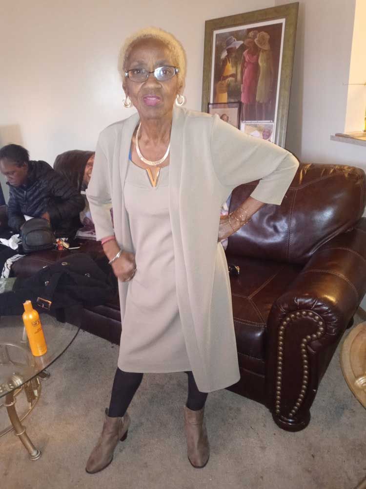 A woman in a dress and cardigan is standing in a living room.