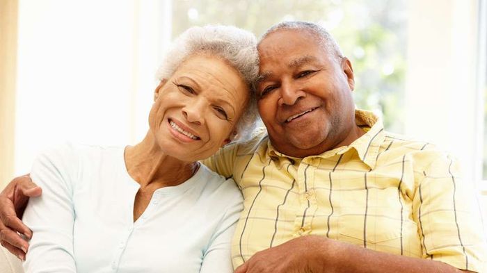 An elderly couple is sitting on a couch and smiling for the camera.