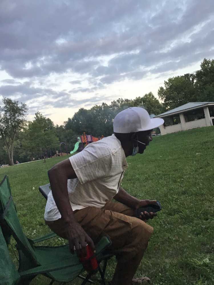 A man in a white hat is sitting in a chair in a park.