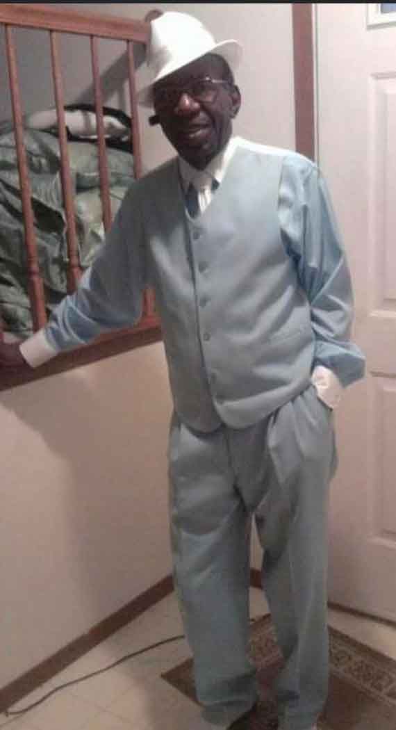 A man in a suit and hat is standing in a hallway.