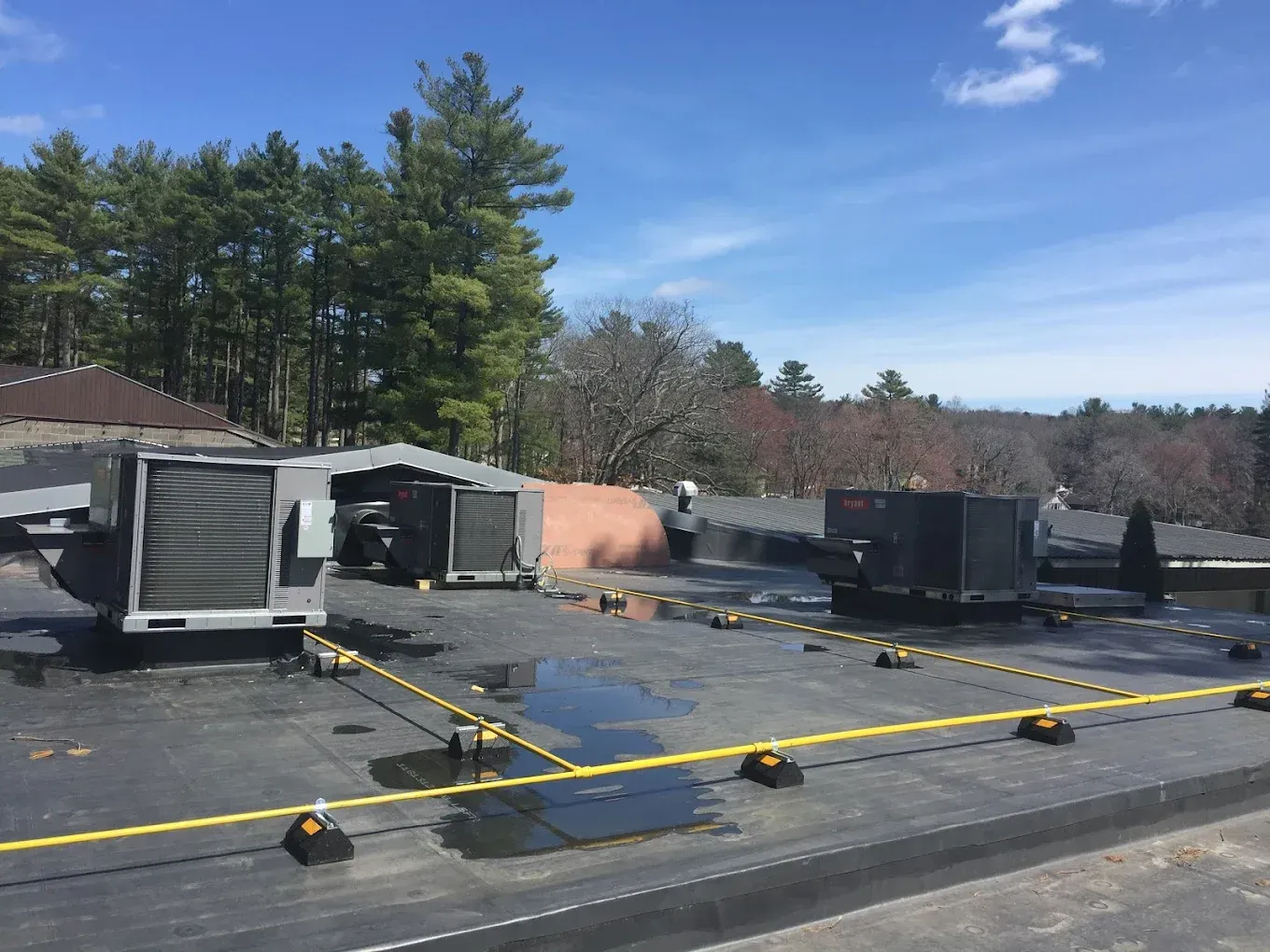 HVAC units on a flat roof with a safety cable system; trees in background on a sunny day.