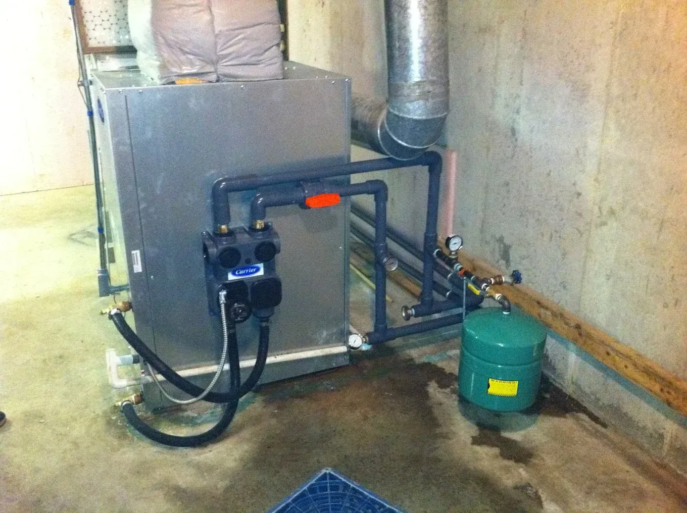 Heating system in a basement with silver unit, black pipes, and green tank.