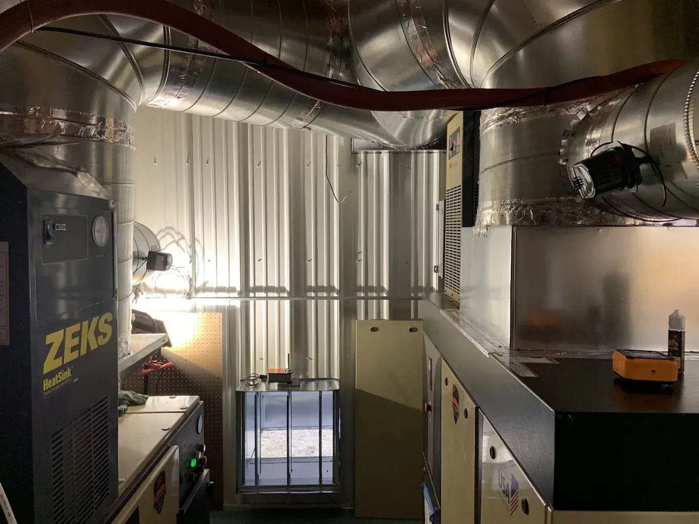 Interior of a mechanical room, featuring air ducts, equipment, and a small doorway.