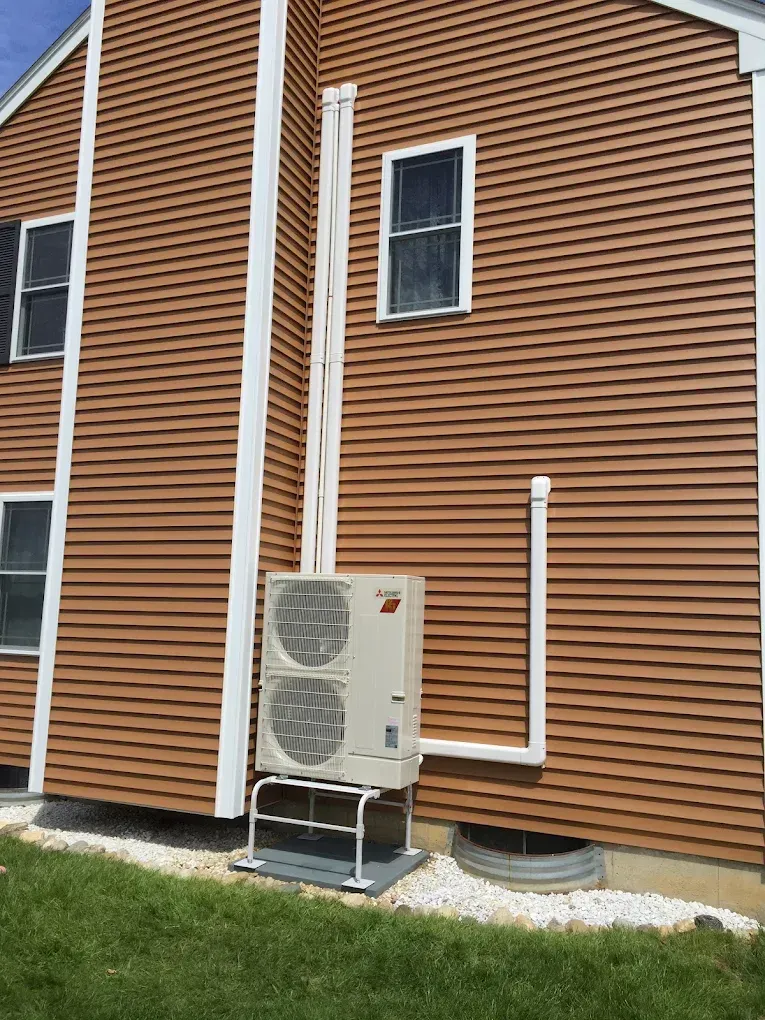 Exterior of a brown house with a white HVAC unit on a metal stand, and white piping.