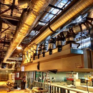 HVAC ductwork in a commercial building under construction. Silver pipes, exposed beams, and construction materials.