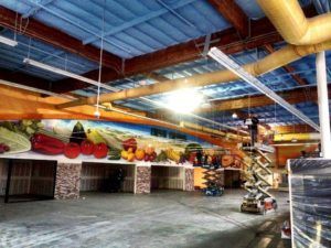 Empty market with a large mural of produce, lit by overhead lights, and a lift platform.