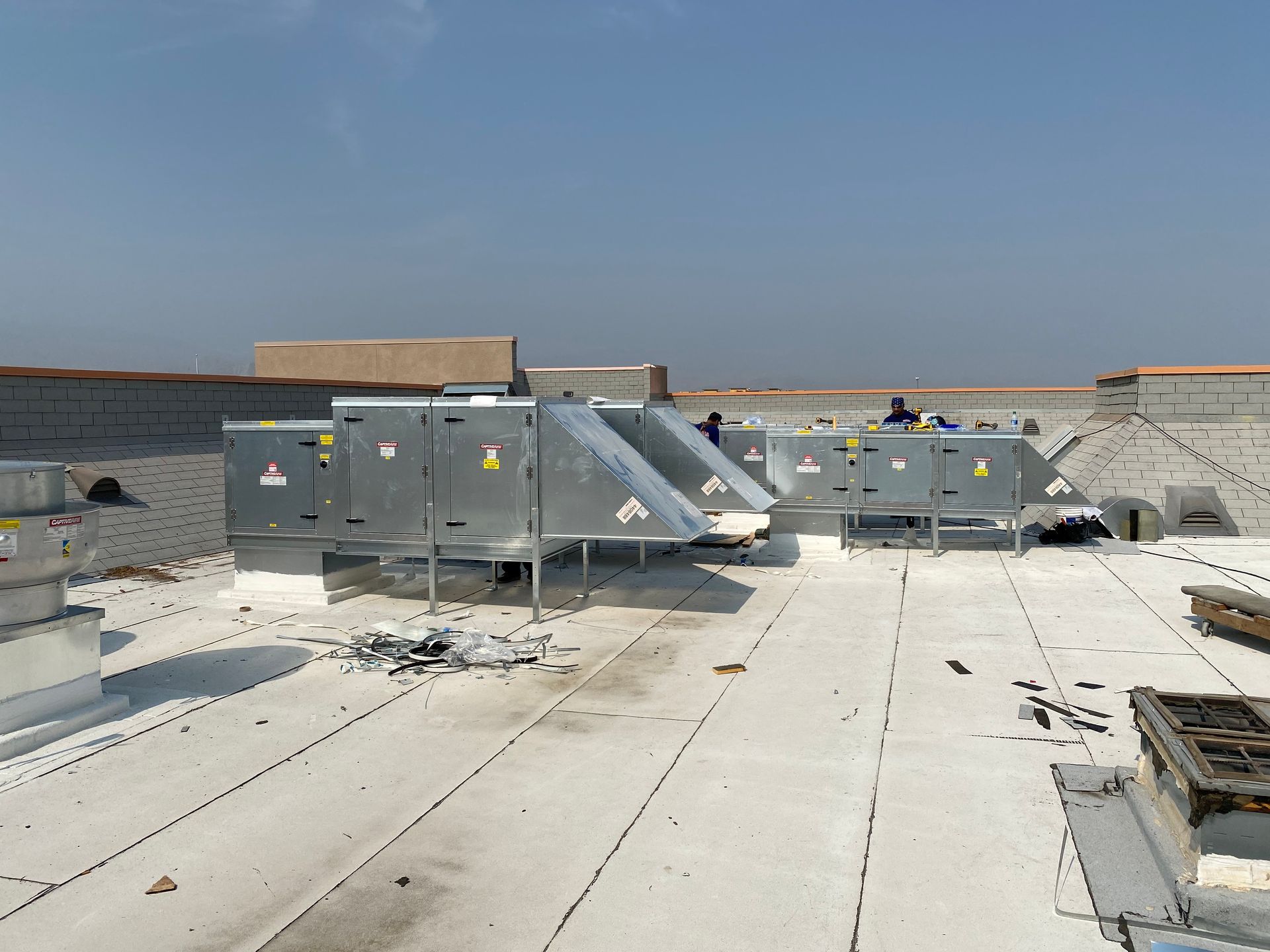 HVAC units on a flat roof with a clear sky. Workers in the background.