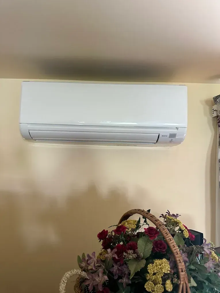 White wall-mounted air conditioner above a basket of flowers on a light yellow wall.