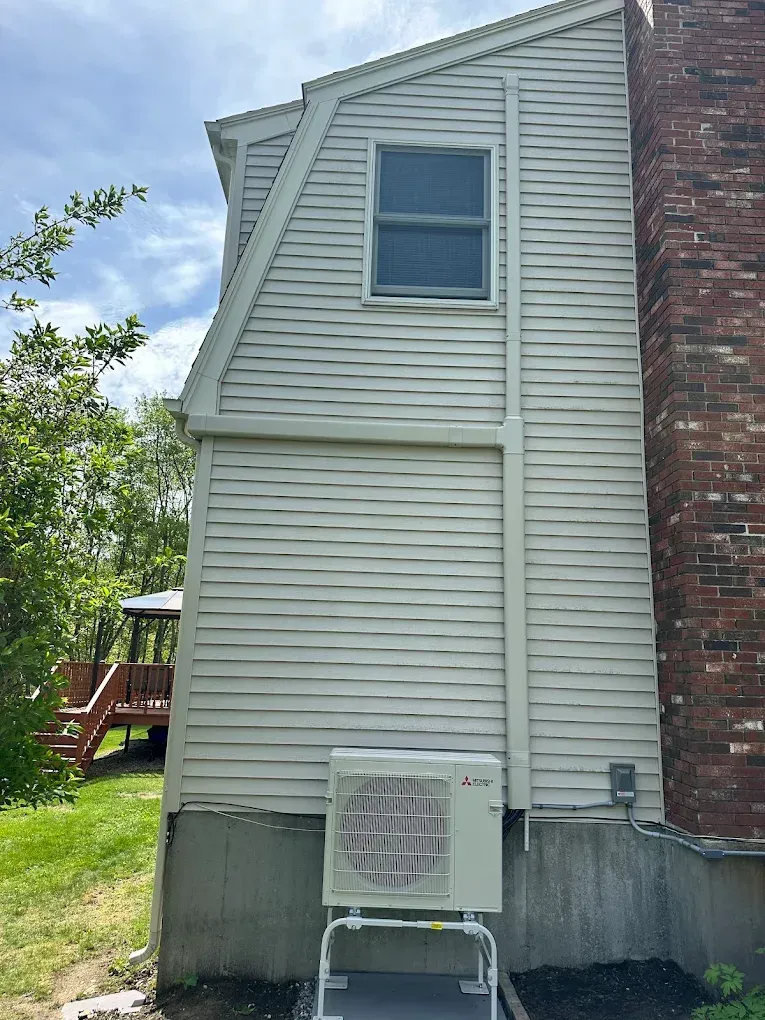 Side of a house with an air conditioning unit and a chimney. Beige siding, blue sky.