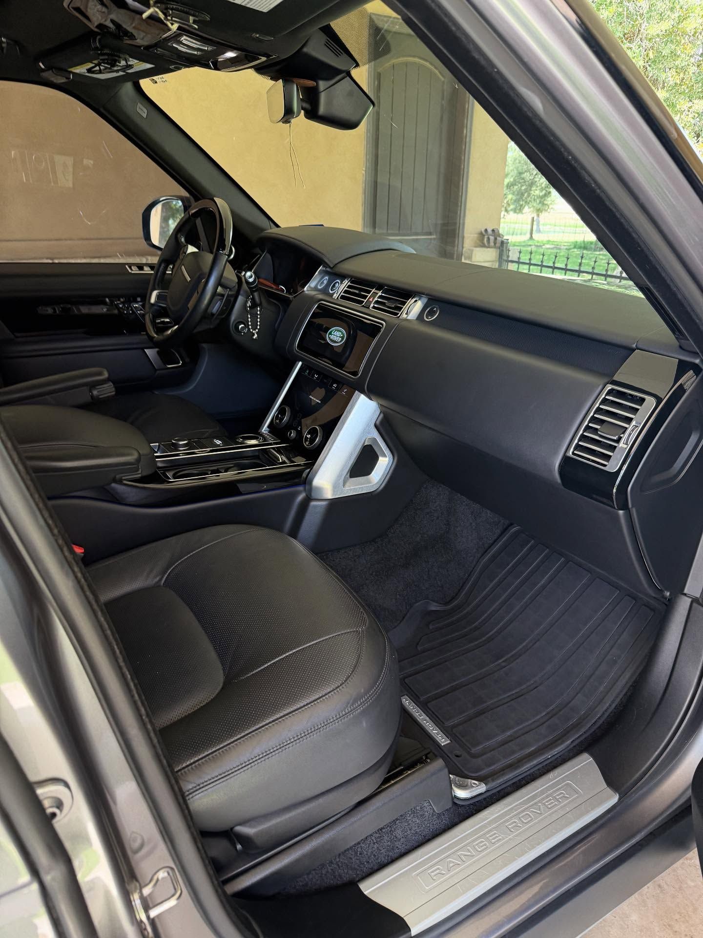 Black leather car interior with open passenger door, dashboard, steering wheel, and silver trim visible