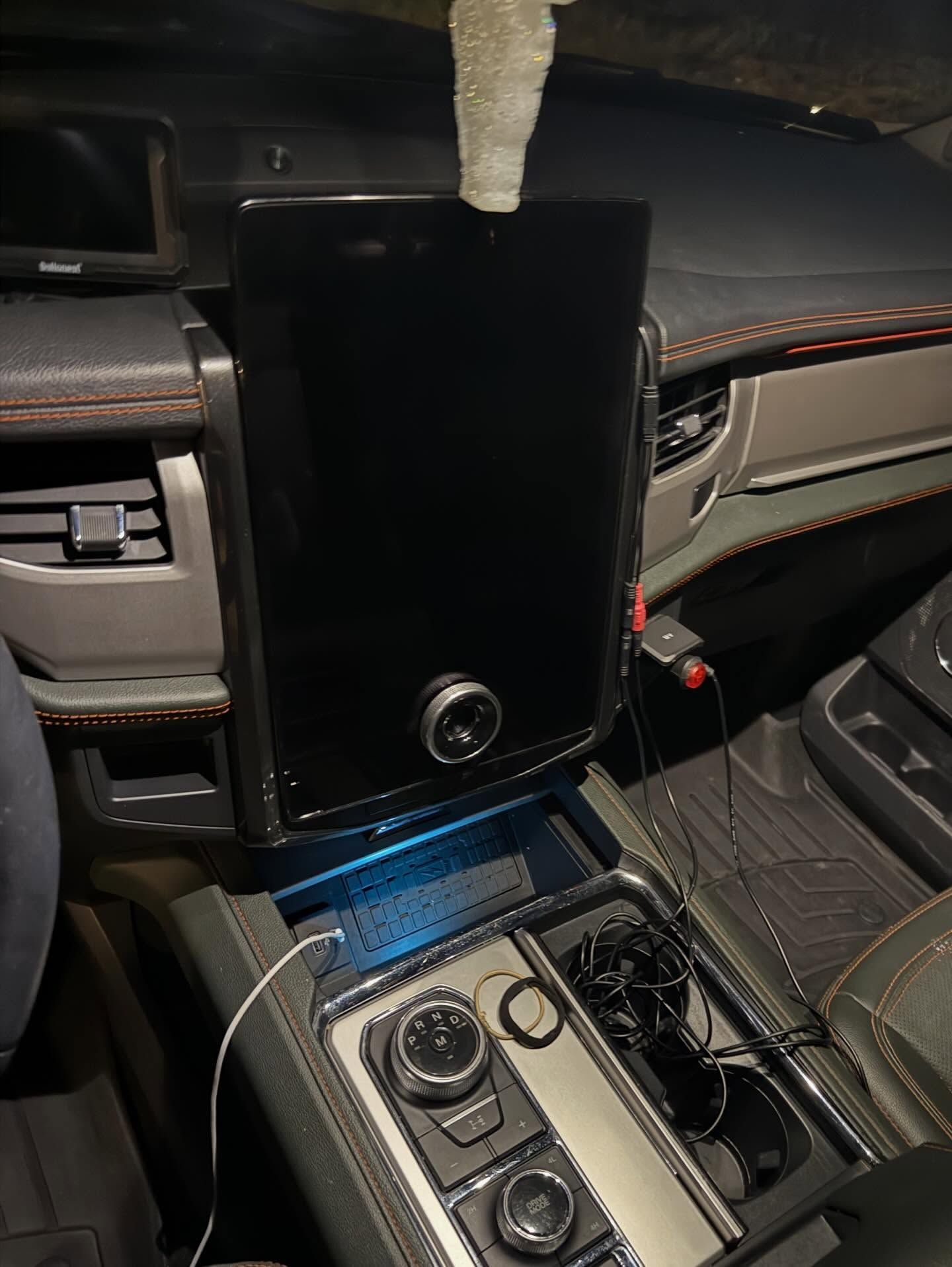 Car dashboard with a large vertical touchscreen and center console controls, lit in blue at night