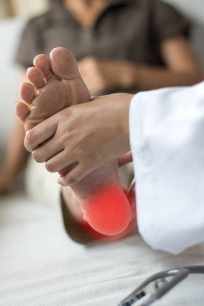 Doctor examining a patient's foot, with red highlighting pain in the heel. The patient sits in a medical setting.