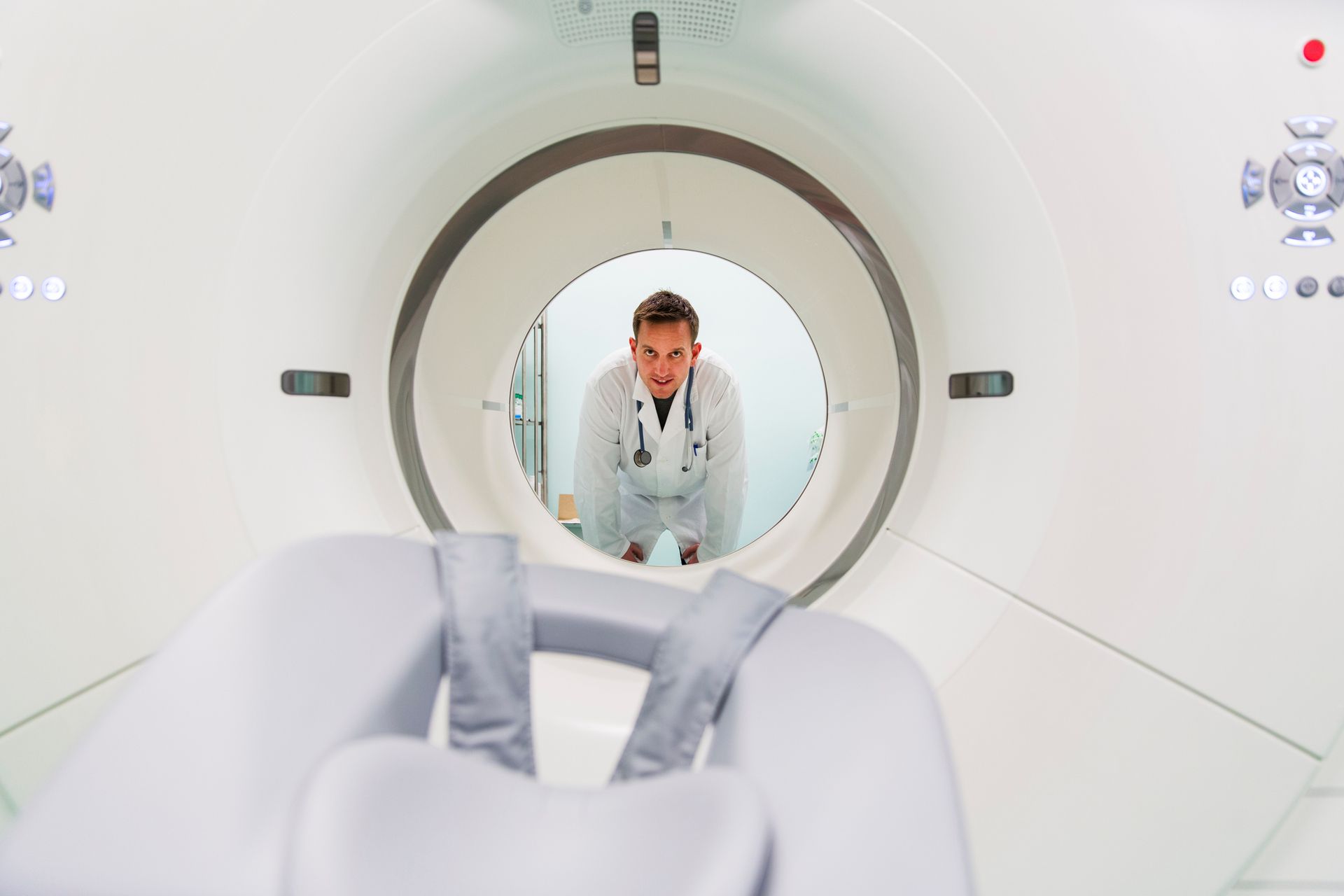 Doctor leans into a CT scanner, looking toward the camera. White medical equipment and setting.