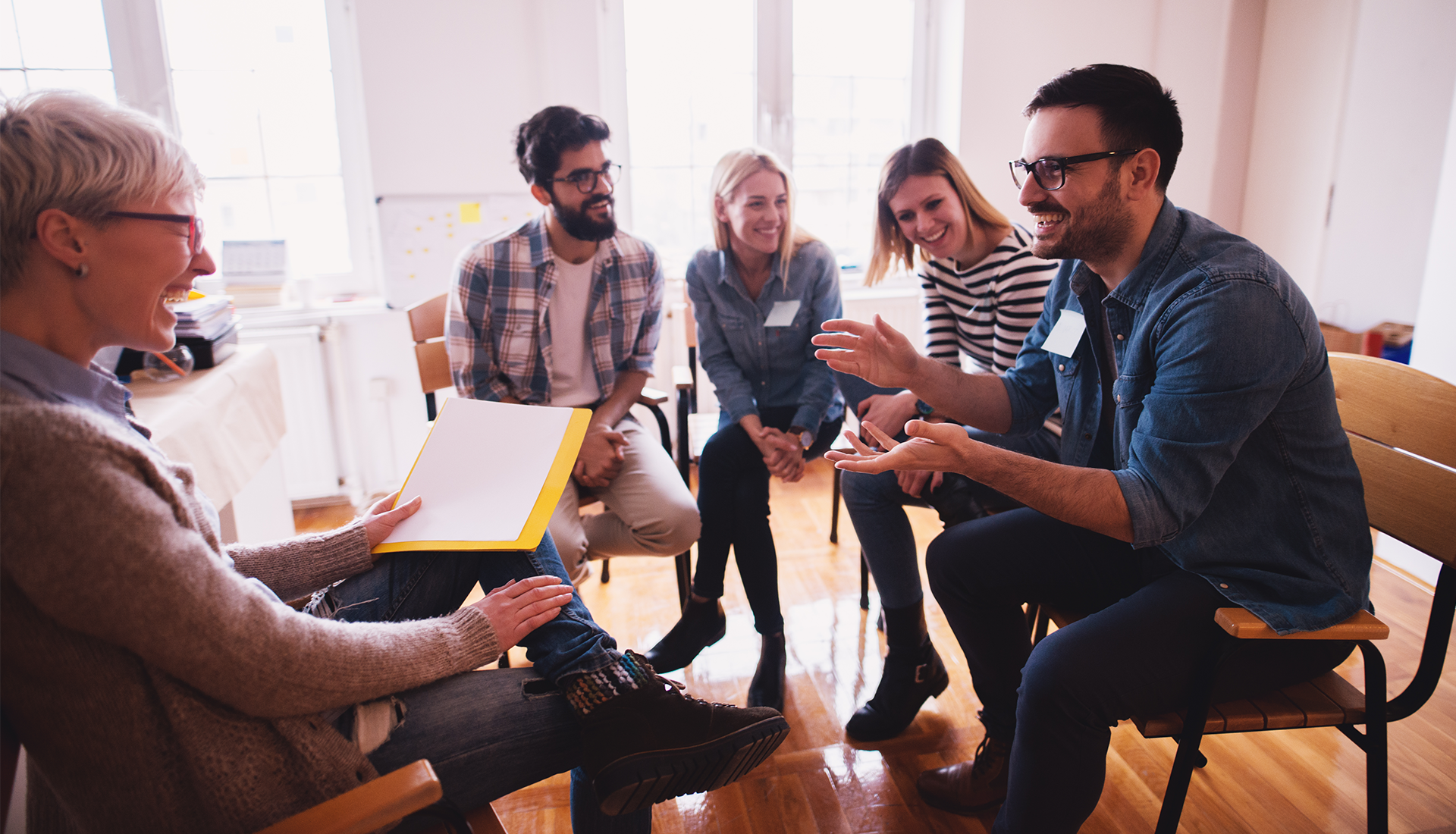 Group therapy session: People seated in a circle, laughing while one man speaks.
