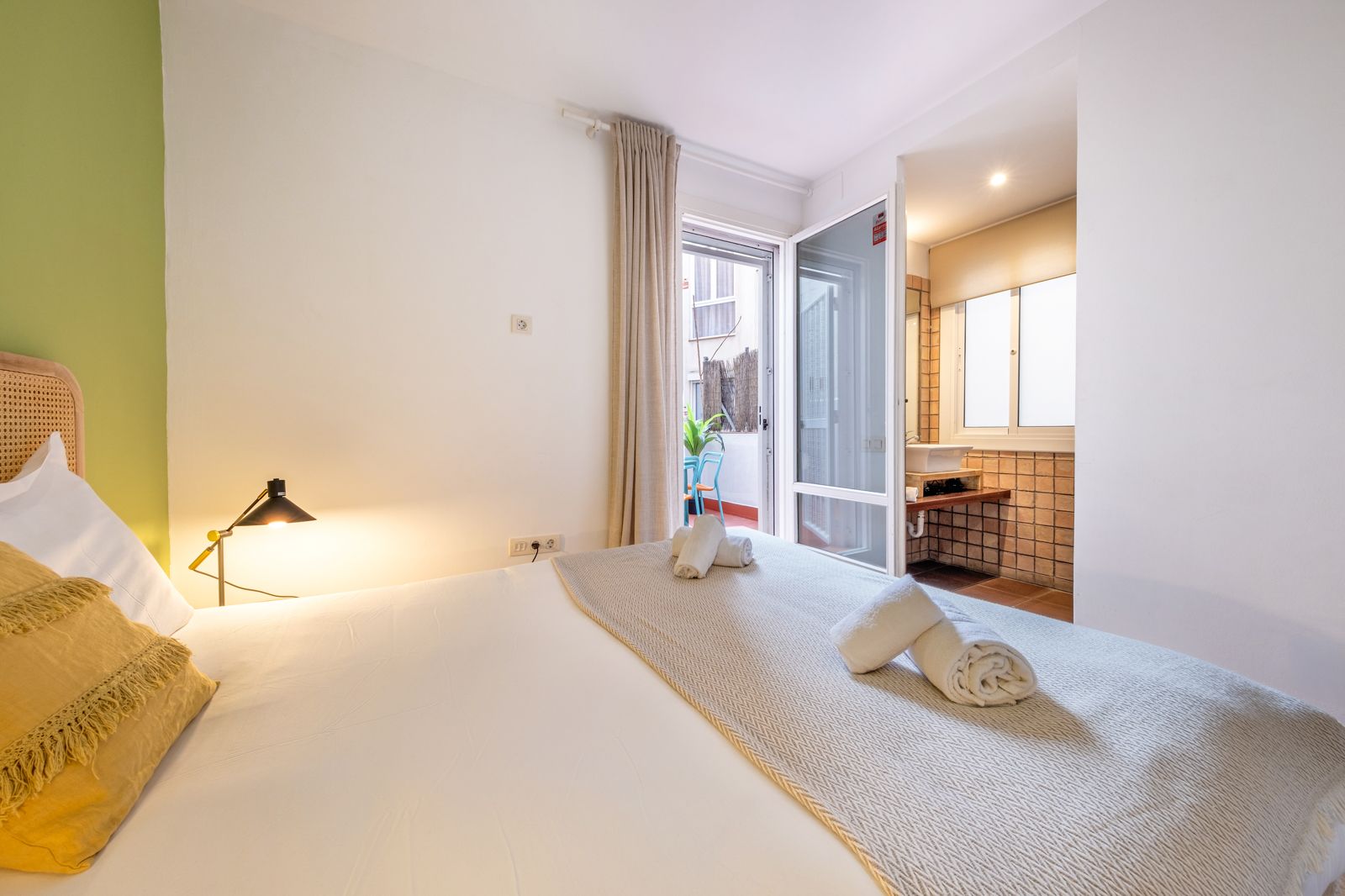 A bedroom with a bed , lamp , towels and a bathroom.
