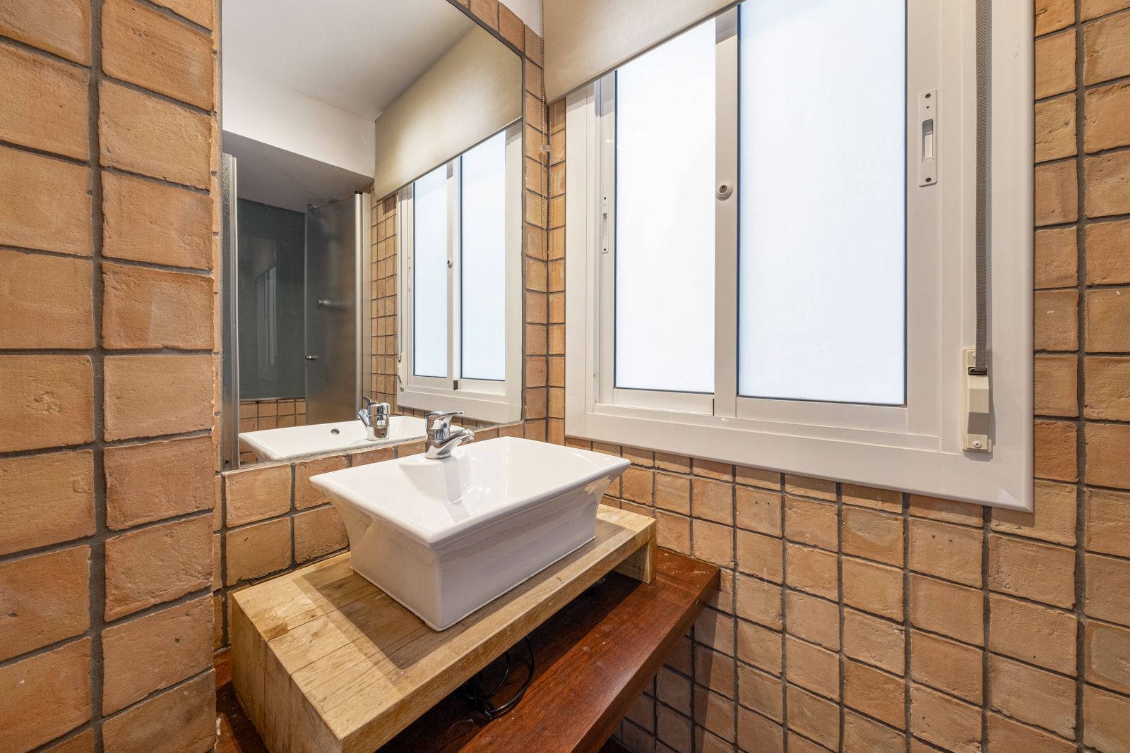 A bathroom with a sink , mirror and window.