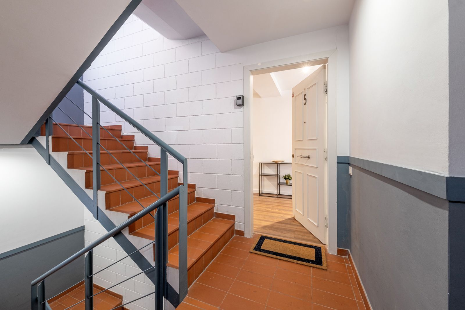 A hallway with stairs and a door leading to a room.