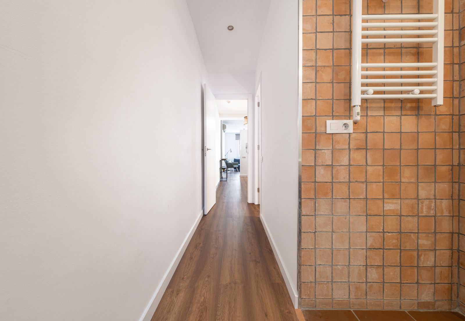 A long hallway with wooden floors and a towel rack on the wall.