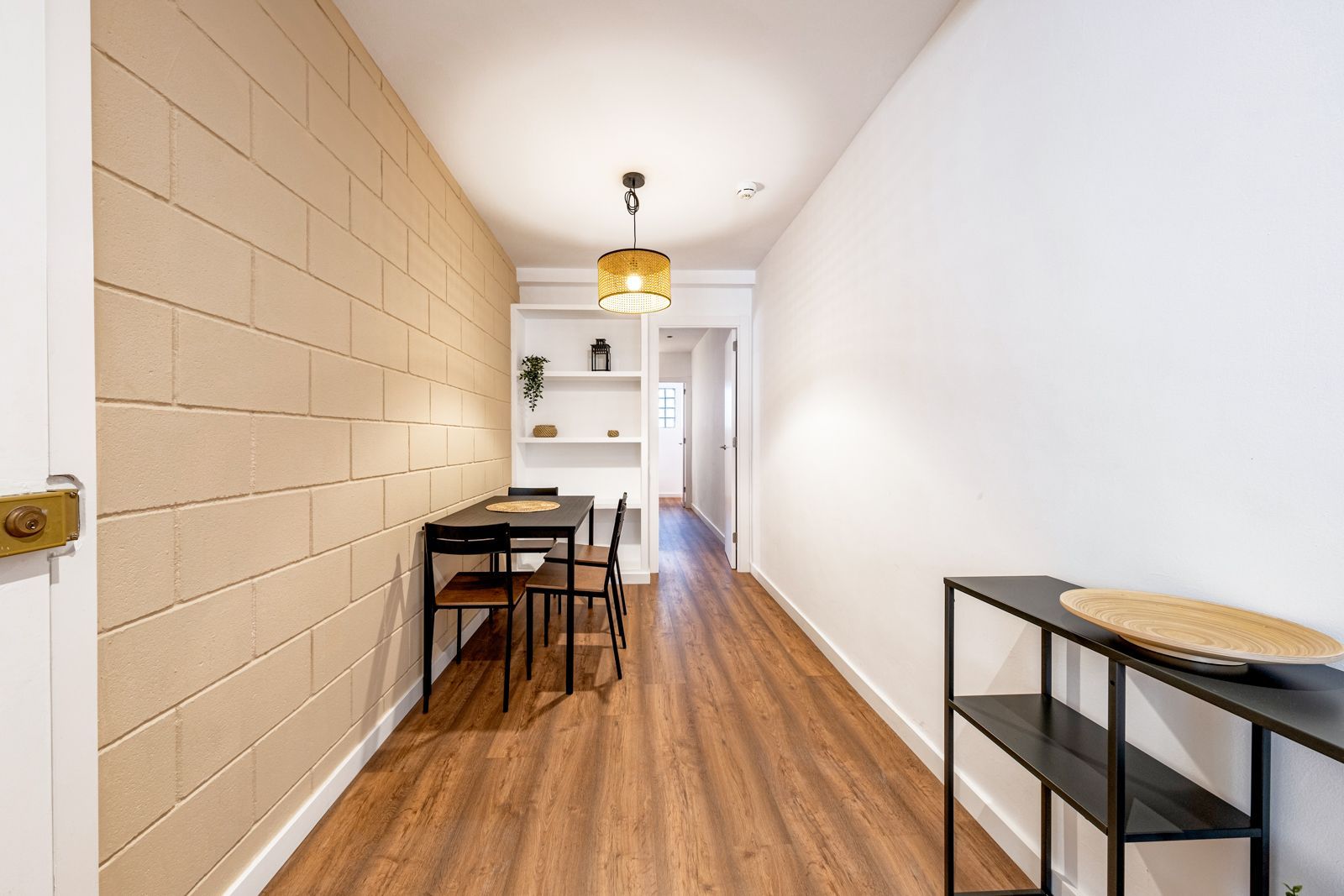 A long hallway with wooden floors and a table and chairs.