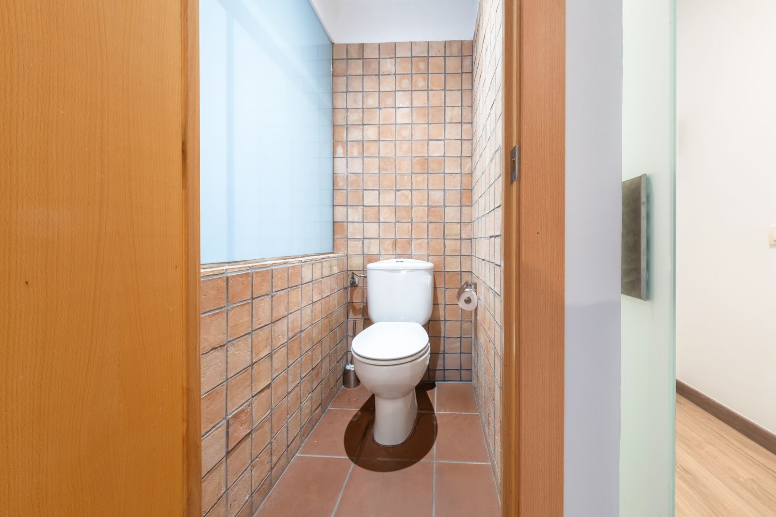 A toilet is sitting in a small bathroom next to a window.