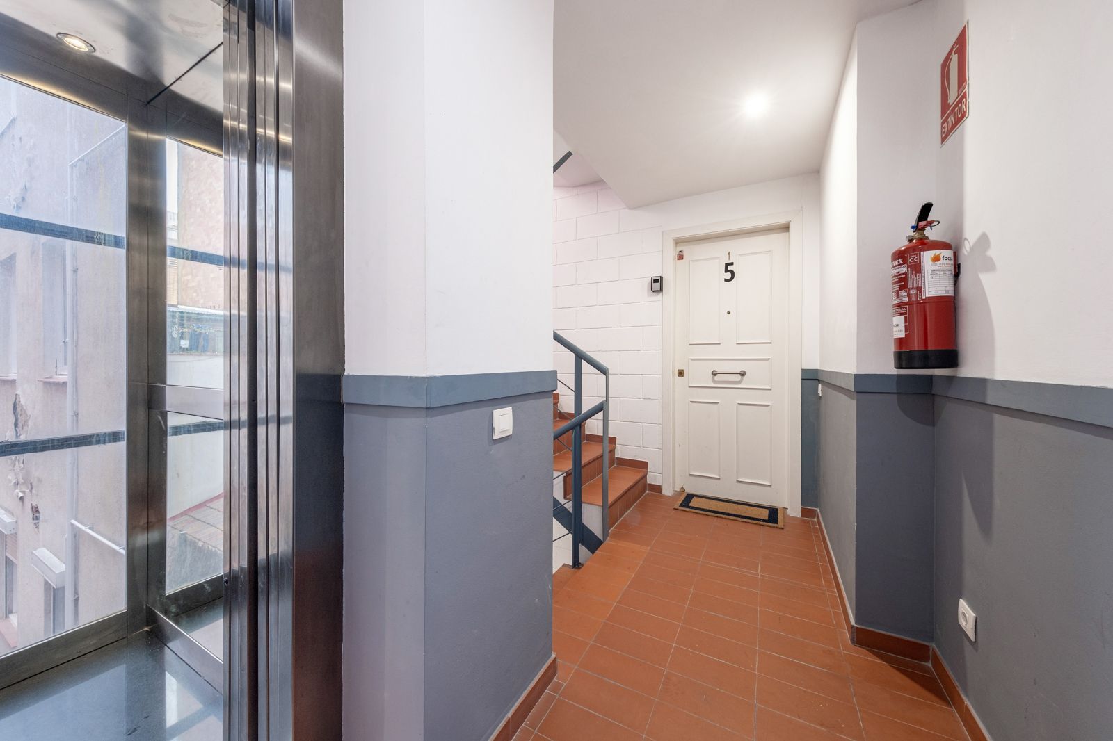 A hallway with stairs and a fire extinguisher on the wall.