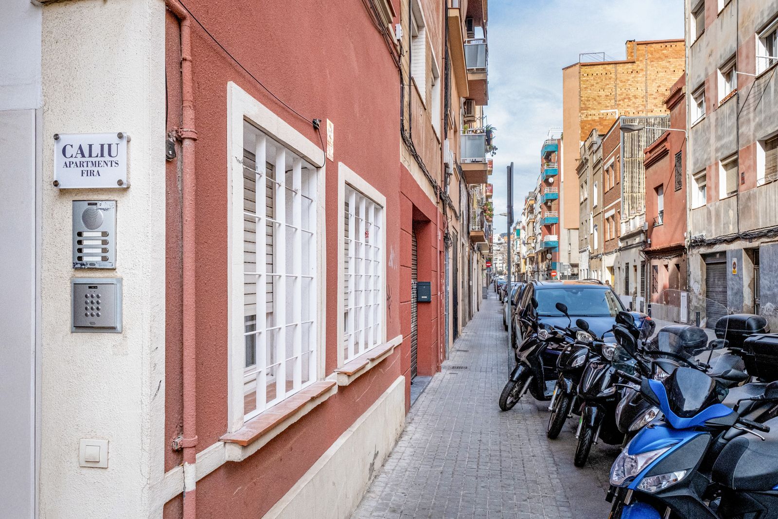 A narrow street with a lot of motorcycles parked on the side of the road.